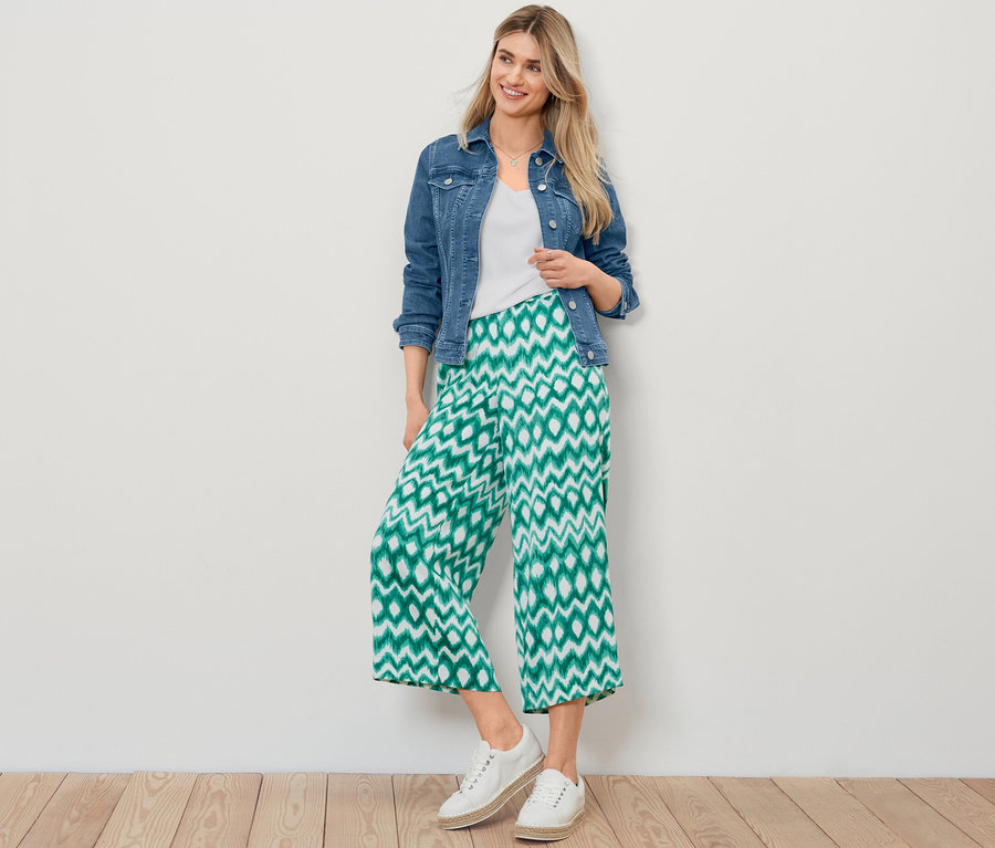 Blondynka pozuje w kurtce dżinsowej, białej koszulce z fakturowaną powierzchnią i wzorzystych satynowych spodniach.