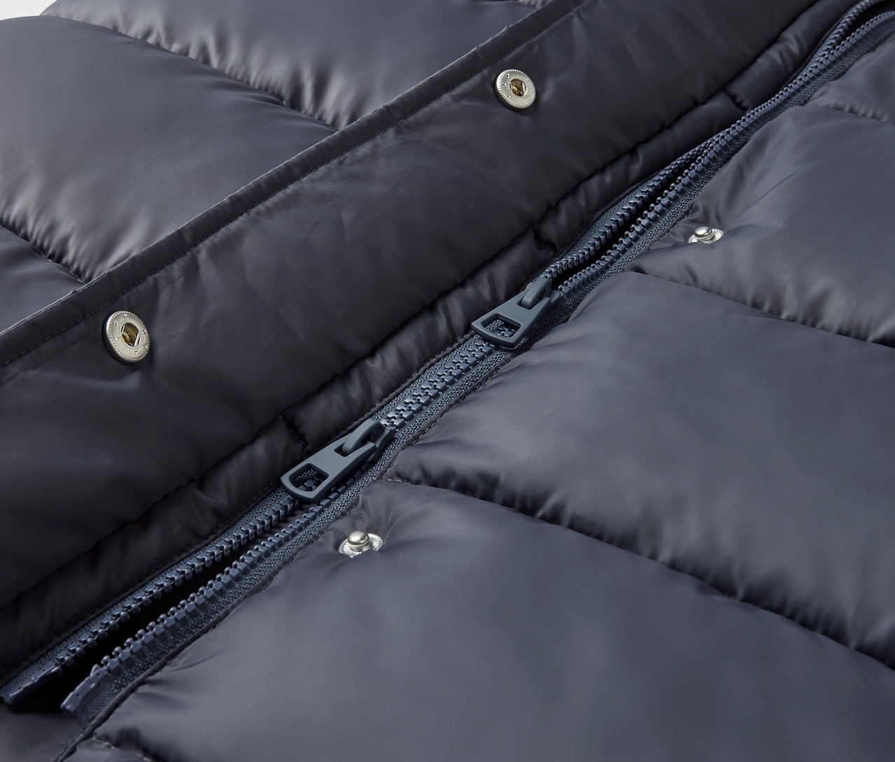 Zbliżenie granatowej kurtki puchowej ze srebrnymi zatrzaskami i zamkiem błyskawicznym.