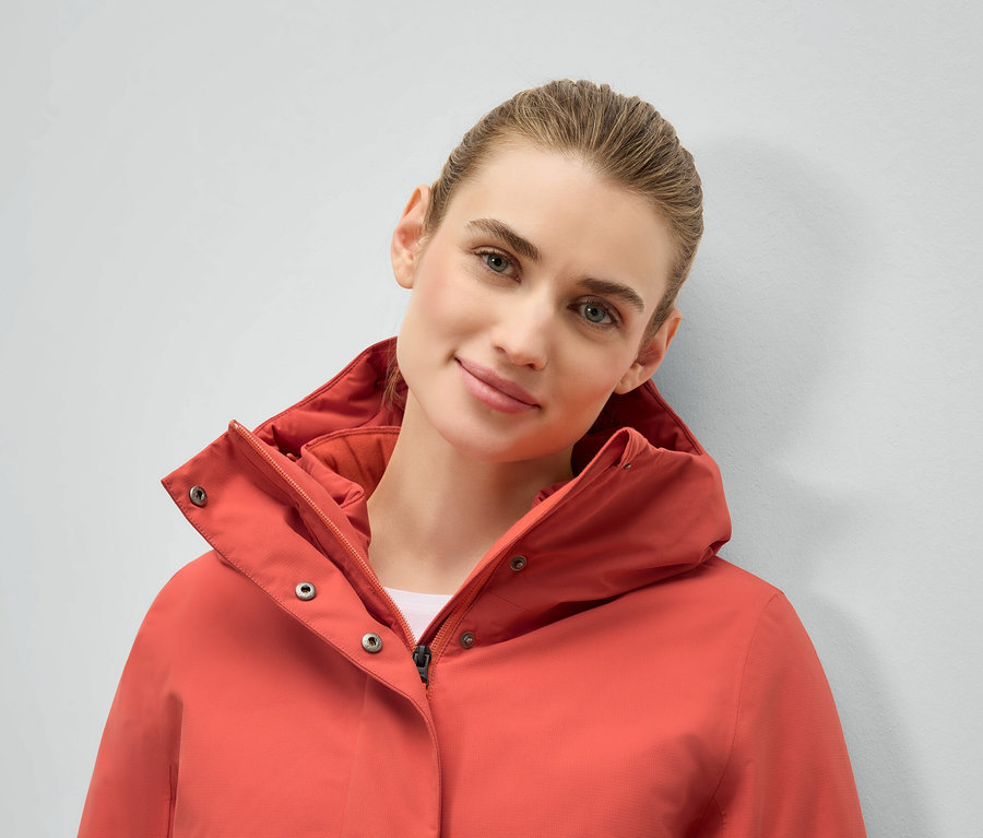 Portret kobiety w koralowej kurtce z kapturem.
