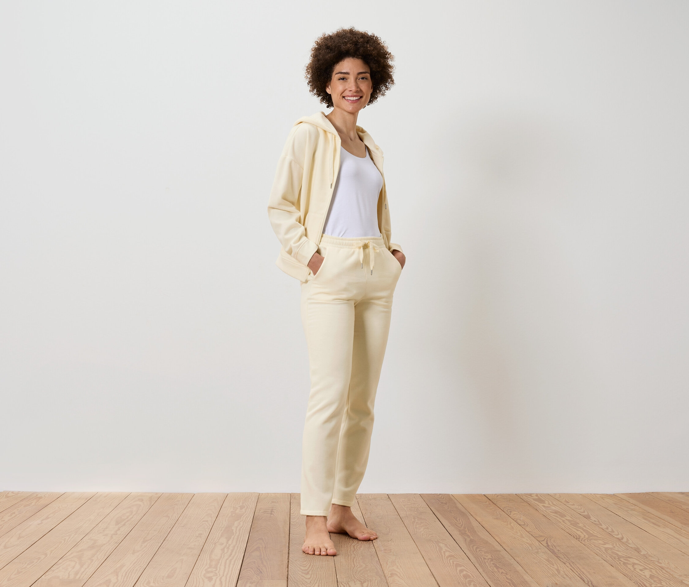 Uśmiechnięta kobieta z fryzurą afro stoi i ma na sobie żółty dres z białym T-shirtem.