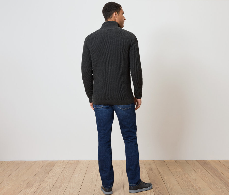 Mężczyzna tyłem do kamery ubrany w ciemnoszary sweter na zamek błyskawiczny, dżinsy i buty.