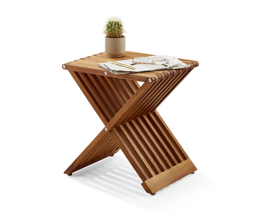 Na składanym hokerze leżą kaktus w doniczce, okulary, pióro i kawałek papieru.