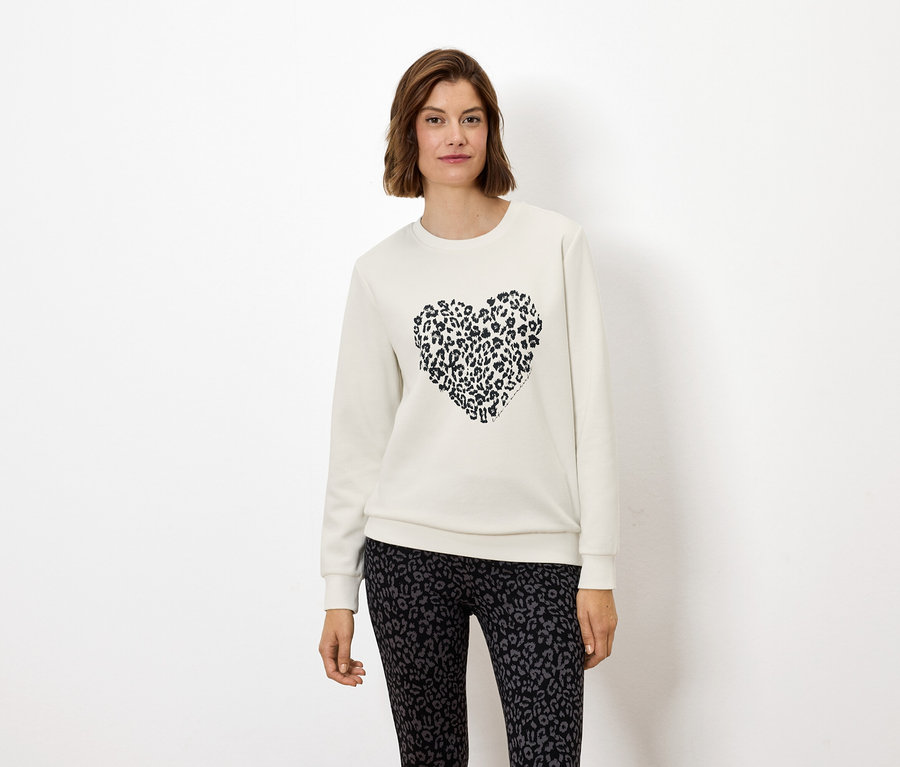 Kobieta ma na sobie białą bluzę z sercem w zwierzęcy wzór i legginsy w zwierzęcy wzór.