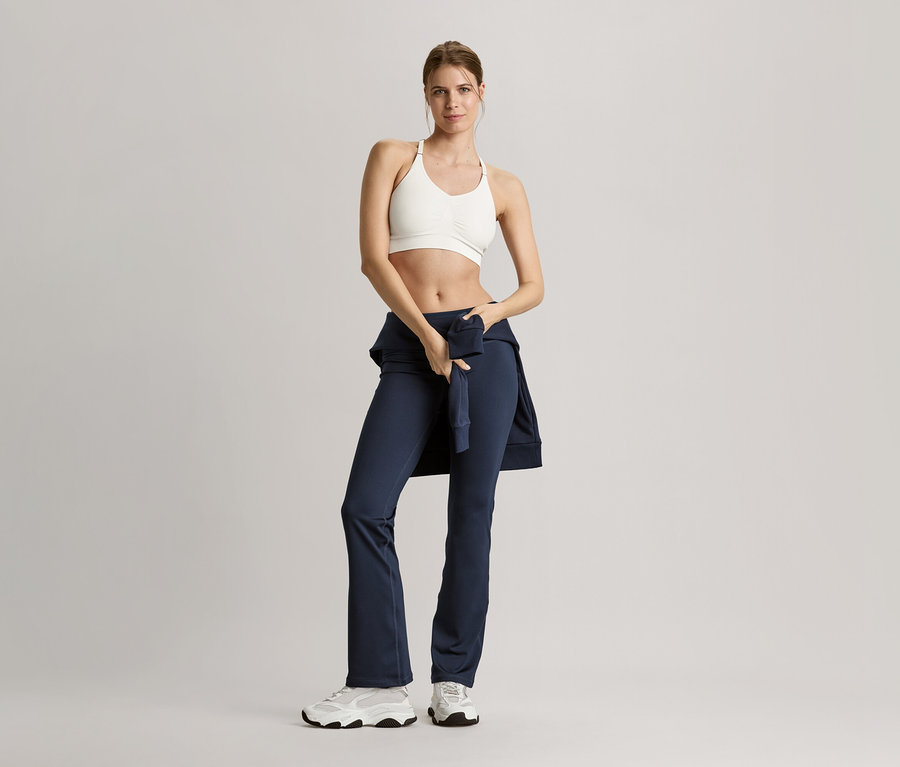 Kobieta w stroju sportowym pozuje z granatową bluzą dresową.