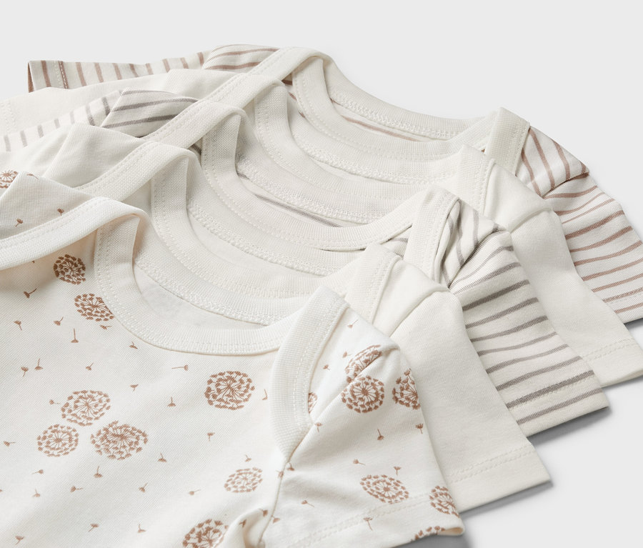 Zbliżenie na pięć body z krótkim rękawem dla niemowląt, w tym jedno z nadrukiem dmuchawca, a inne w paski.