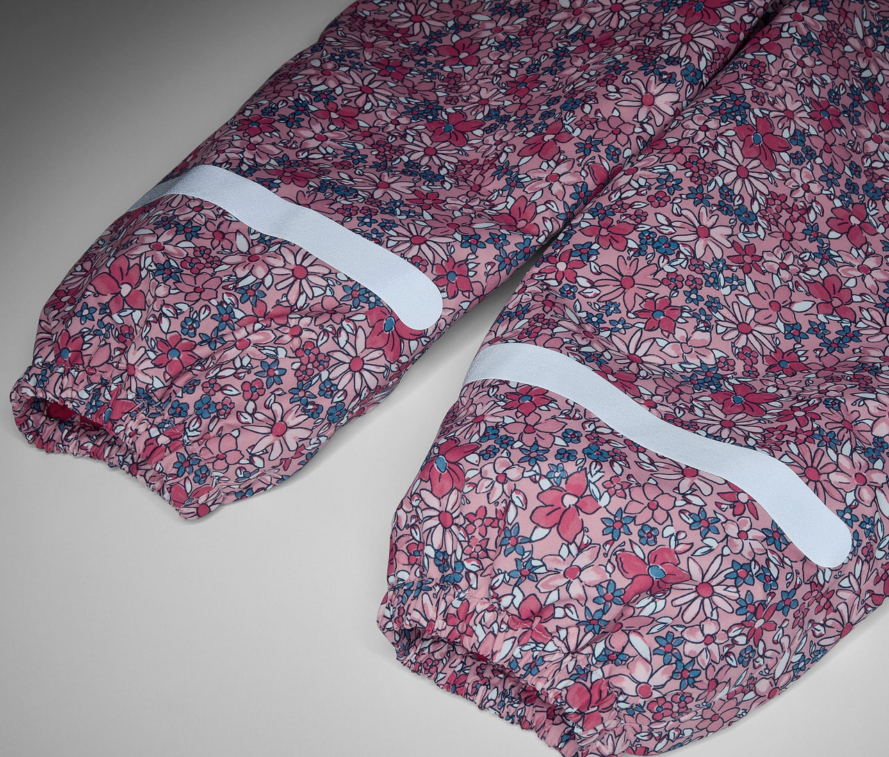 Zbliżenie na termoaktywne spodnie przeciwdeszczowe w kwiaty z paskami odblaskowymi.