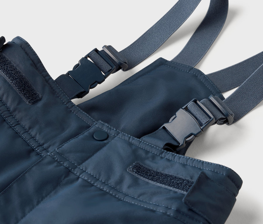 Zbliżenie na niebieskie spodnie na szelkach z szarymi paskami i plastikowymi klamrami.