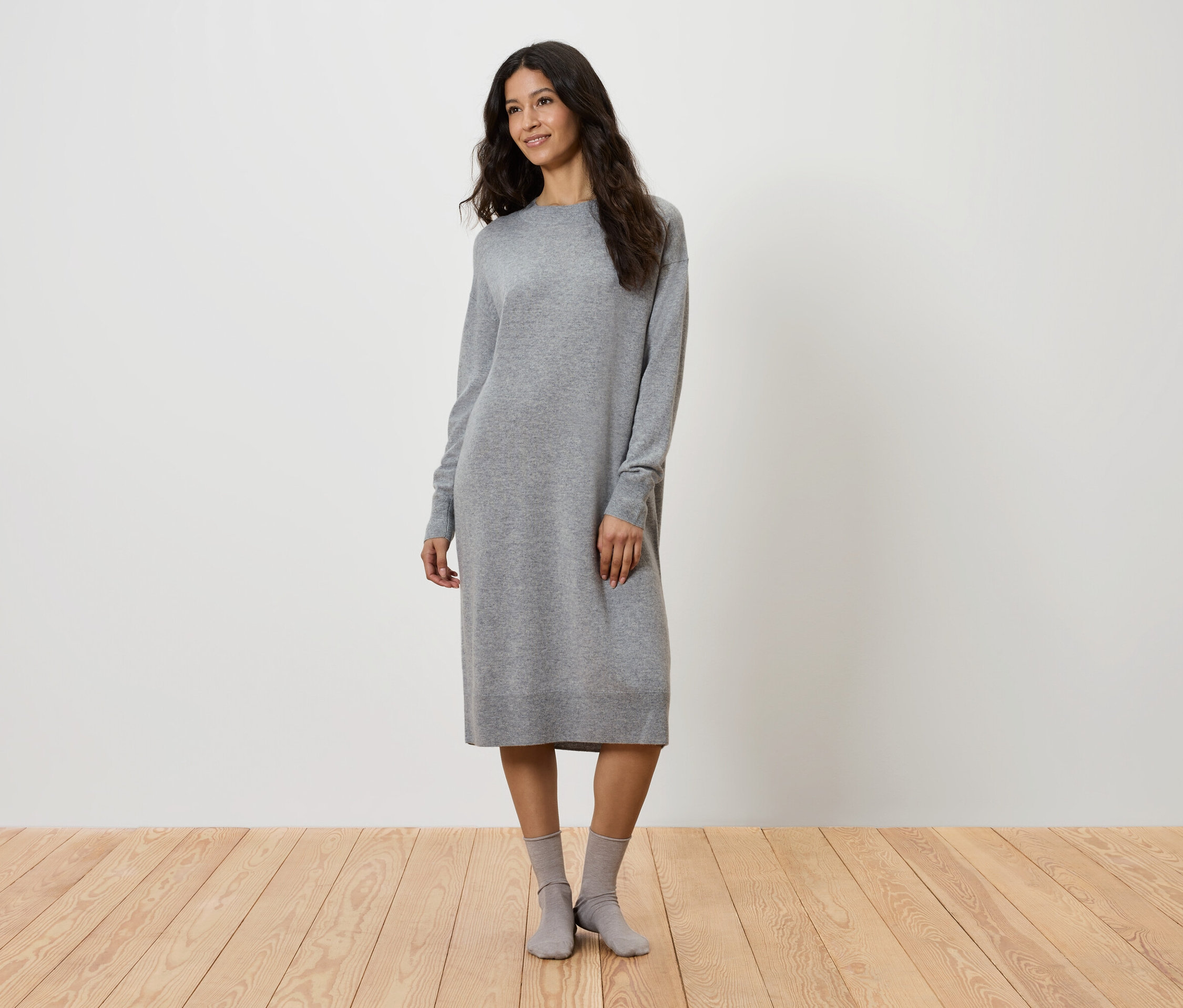 Kobieta stoi w szarej dzianinowej sukience i szarych skarpetach.