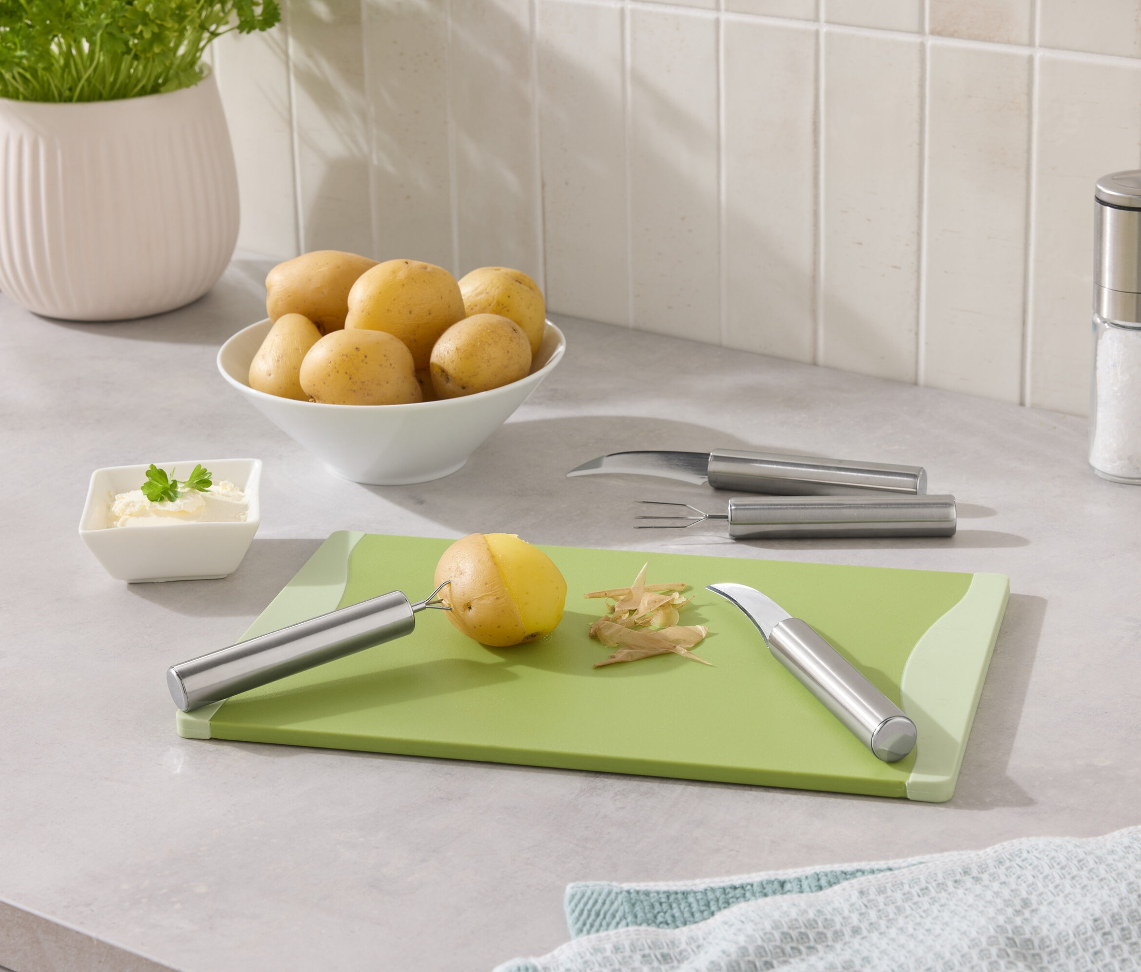 Ziemniaki w misce i jeden ziemniak obrany na zielonej desce.