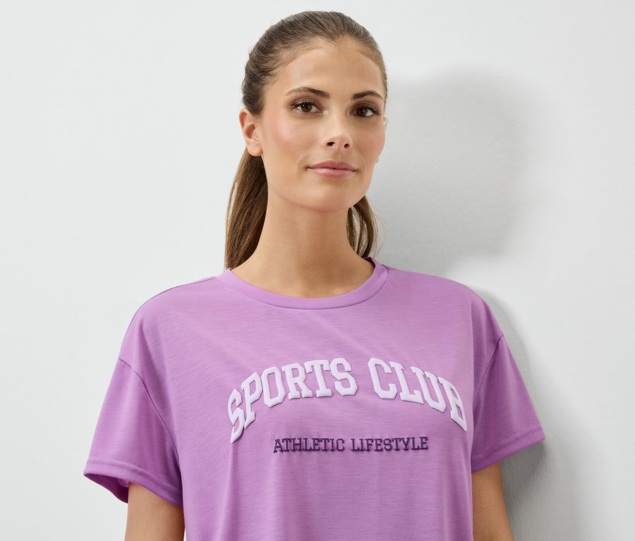 Kobieta w liliowej koszulce z napisem SPORTS CLUB ATHLETIC LIFESTYLE.
