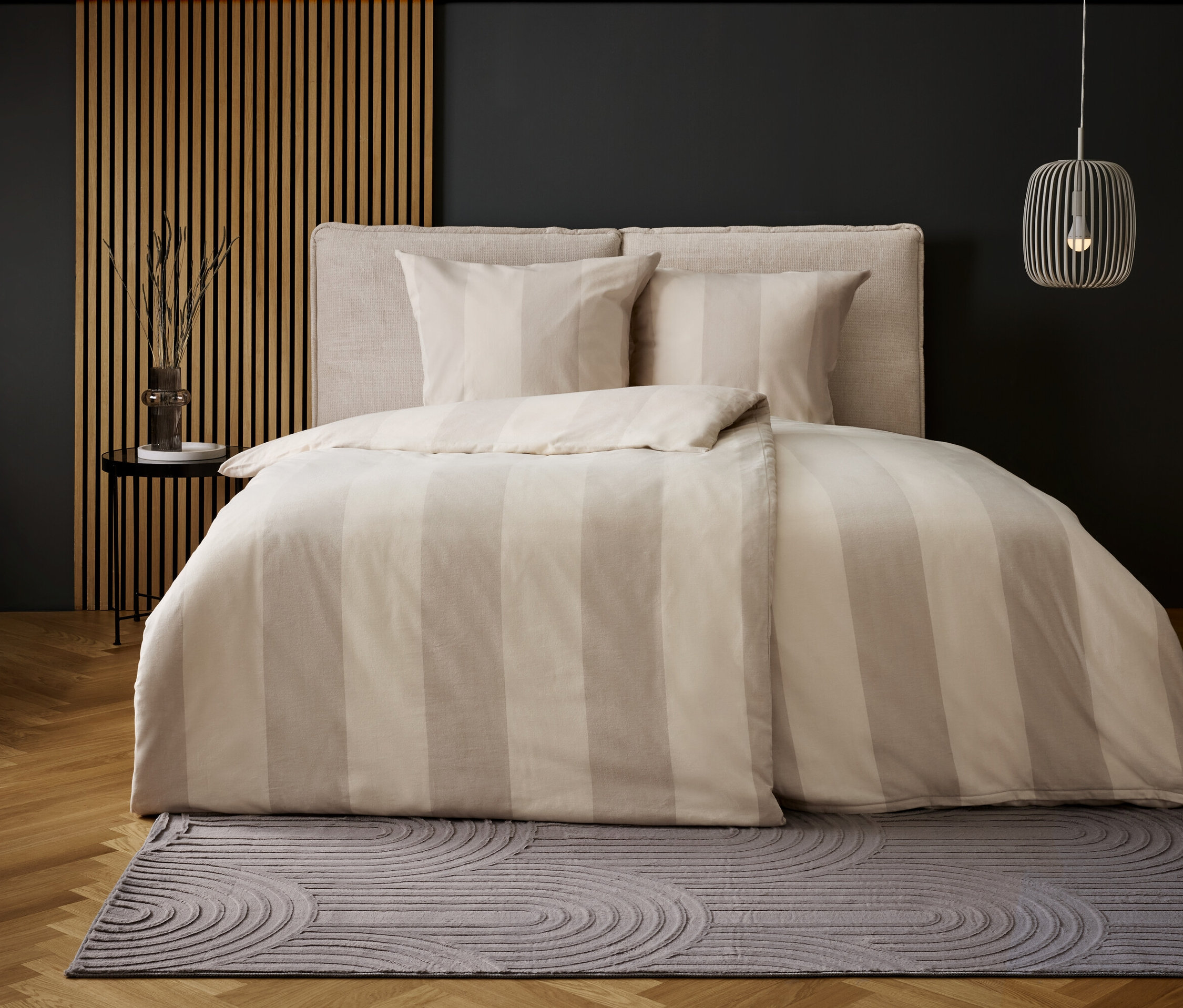 Sypialnia z pościelą w beżowe paski i szarym dywanem z okrągłym wzorem.