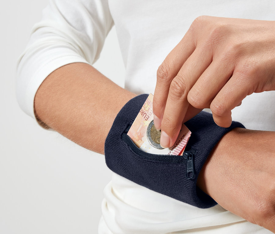 Osoba wkłada monetę euro do granatowej opaski na nadgarstek.