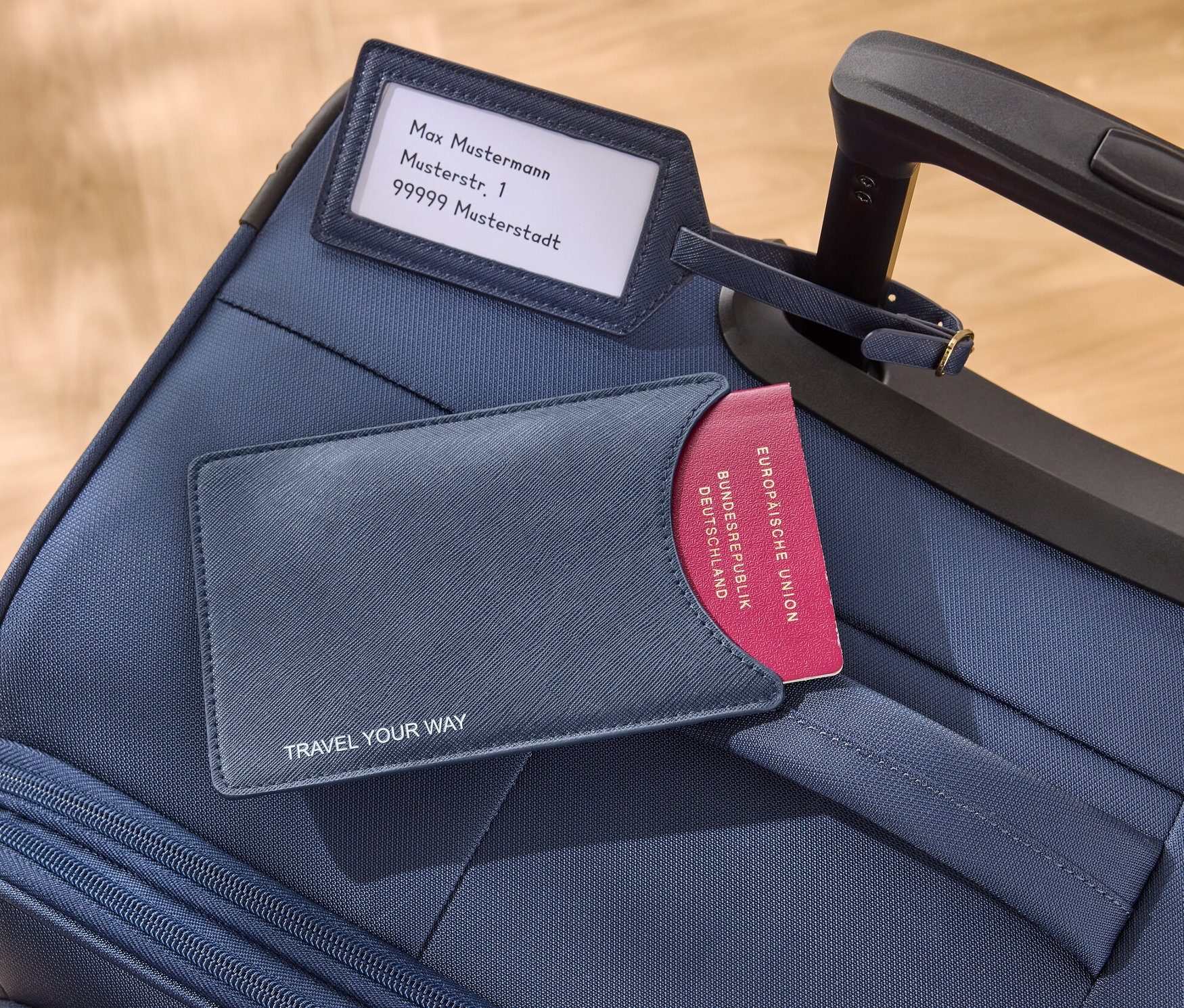 Na niebieskiej walizce leżą niebieska okładka na paszport i przywieszka do bagażu.