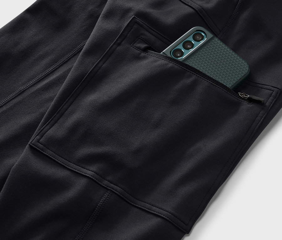 Zbliżenie na czarne legginsy outdoorowe z kieszenią, w której znajduje się zielony telefon komórkowy.