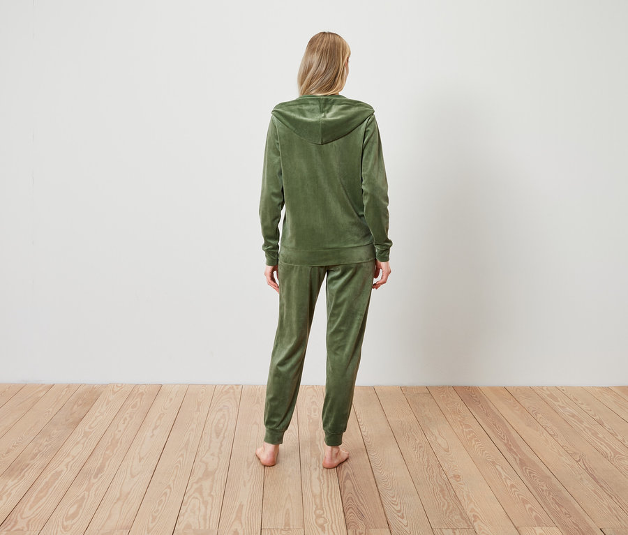 Kobieta stoi tyłem do kamery, ubrana w oliwkowozielony welurowy dres.