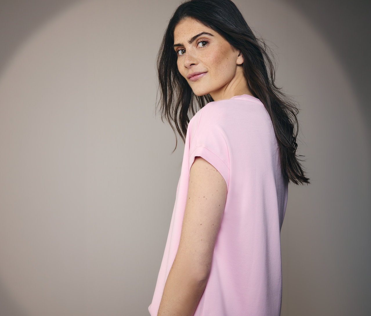 Kobieta w koszulce z nadrukiem CECIL, spogląda przez ramię.