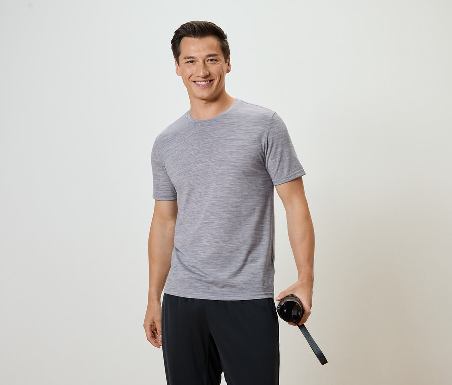 Mężczyzna w szarej koszulce i czarnych spodniach trzyma butelkę wody.