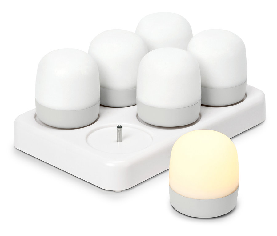 Pięć białych, okrągłych lampek nocnych w stacji ładującej, obok stoi kolejna świecąca lampka nocna.