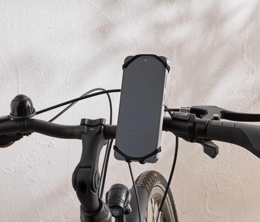 Zbliżenie kierownicy roweru ze smartfonem przymocowanym gumką.