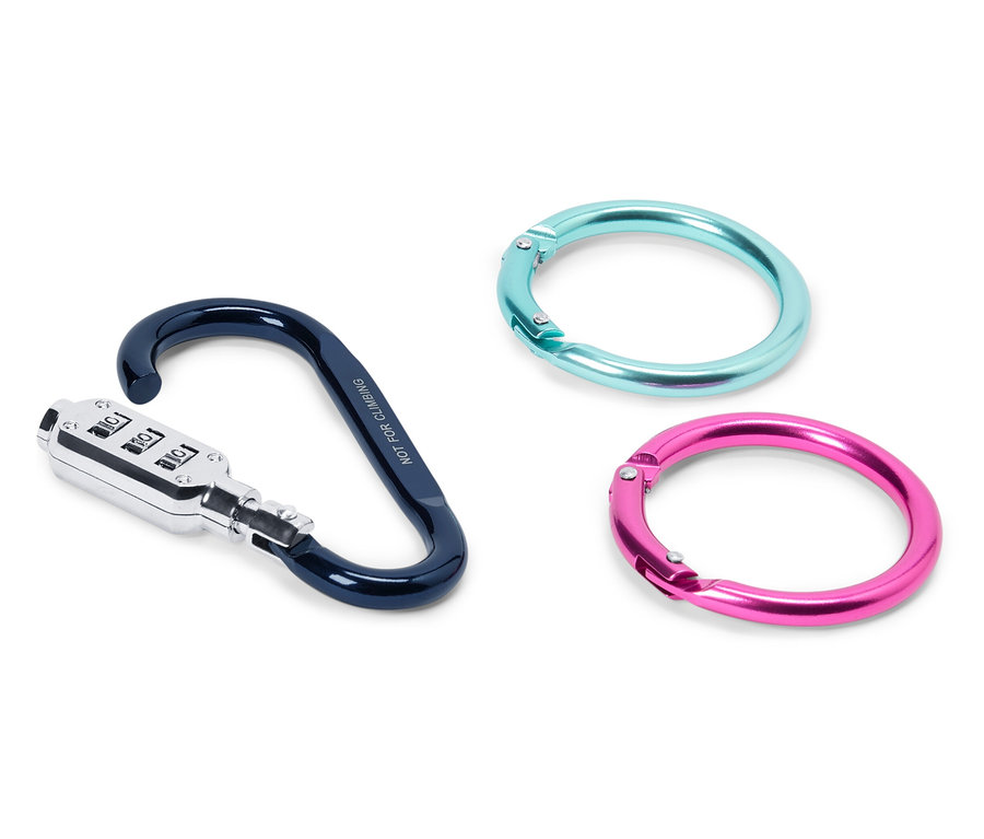 Trzy przedmioty leżą na białej powierzchni: karabińczyk z zamkiem szyfrowym w kolorze czarno-srebrnym oraz dwa pierścienie, jeden turkusowy, drugi różowy.