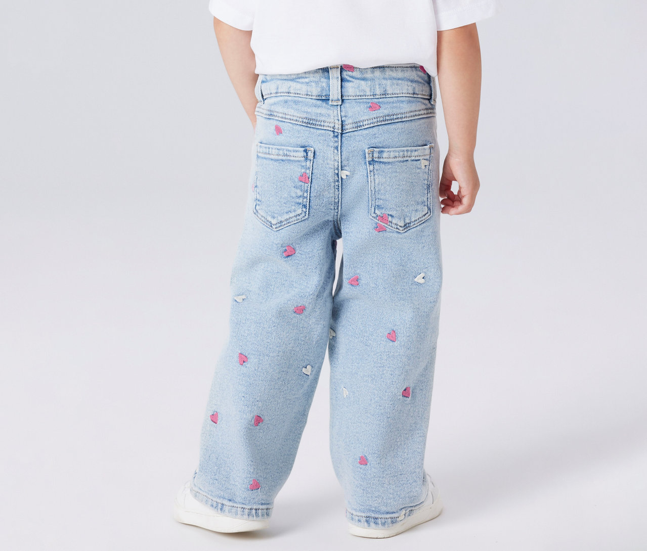 Dziecko od tyłu w dziecięcych jeansach Wide Leg NAME IT z motywem serca i białych butach.