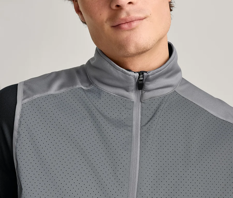 Zbliżenie mężczyzny w szarej kamizelce zapinanej na zamek błyskawiczny, założonej na czarną koszulę z długim rękawem.