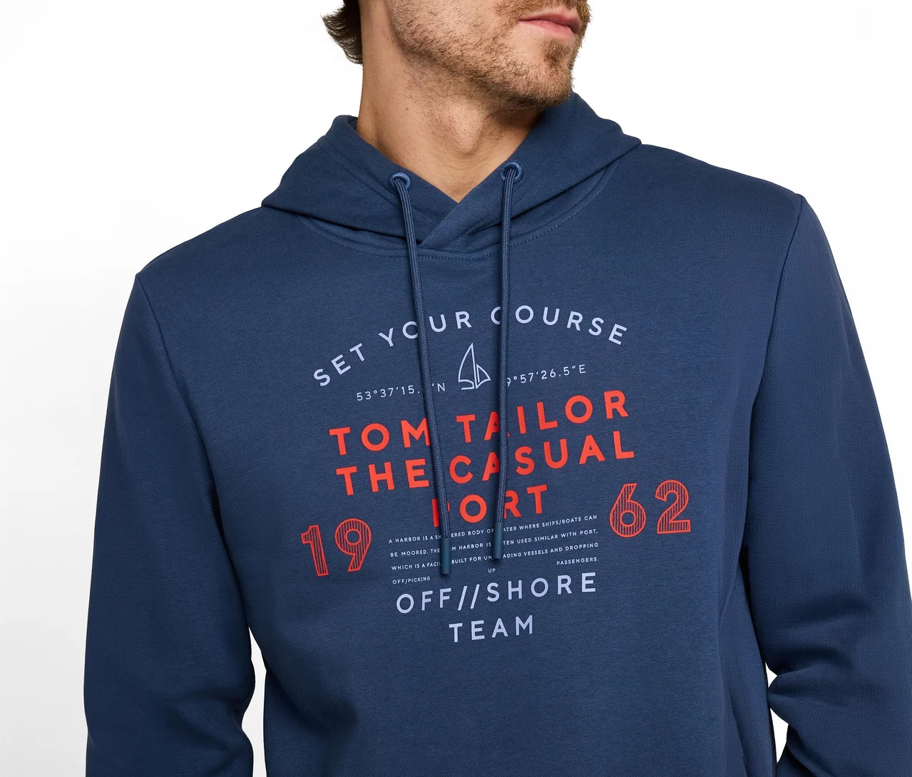 Mężczyzna w granatowej bluzie z kapturem z graficznym nadrukiem. Nadruk zawiera tekst „SET YOUR COURSE”, „TOM TAILOR THE CASUAL”, „OFF//SHORE TEAM”, symbol żaglówki oraz liczby 19 i 62.