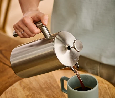 Kobieta nalewa kawę z dwuściankowego zaparzacza tłokowego ze stali nierdzewnej o pojemności 900 ml do filiżanki.