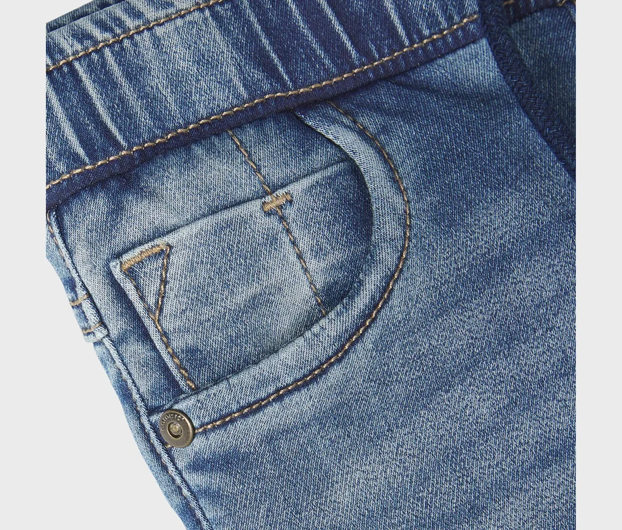 Zbliżenie na niebieskie dżinsy NAME IT Slim Sweat Jeans, z elastycznym pasem, przednią kieszenią, małą kieszonką i metalowym guzikiem z napisem „NAME IT”.