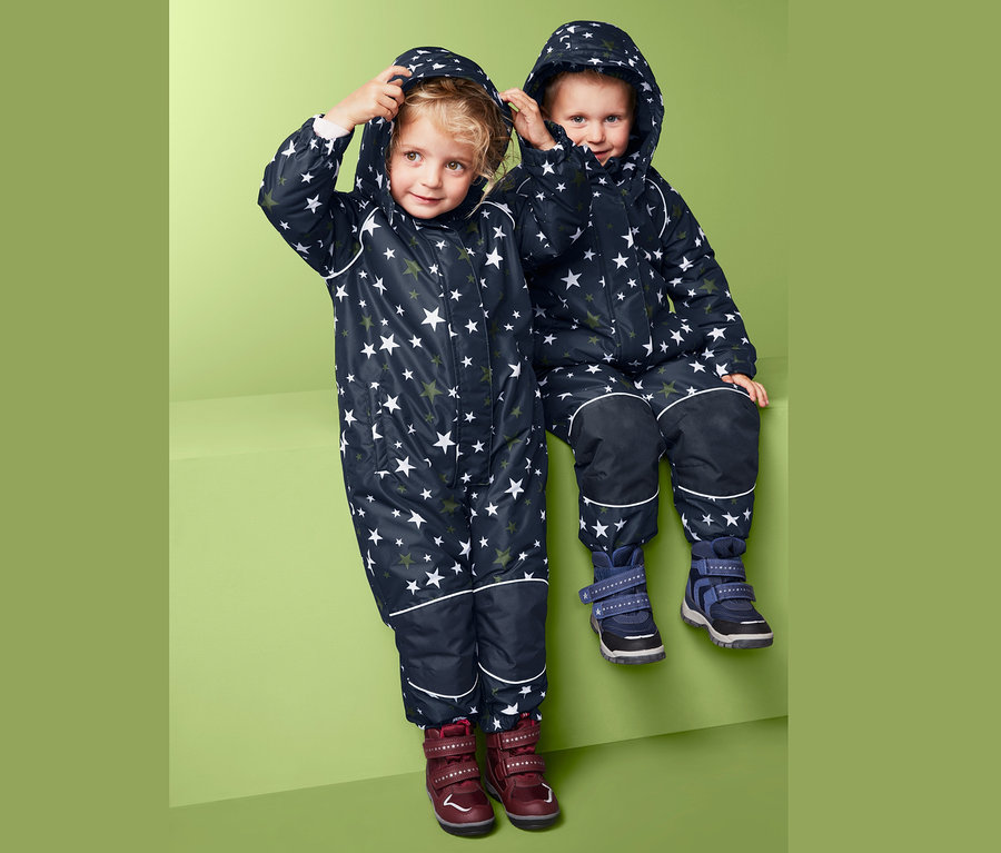 Dzieci w kombinezonach zimowych w gwiazdy siedzą obok siebie.