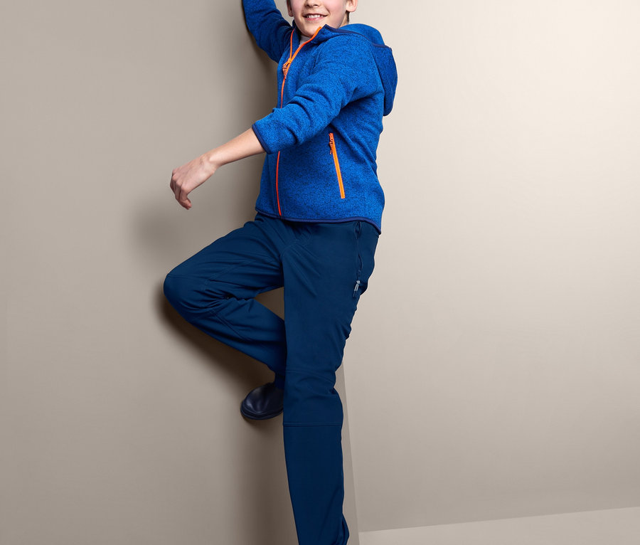 Chłopiec wspina się po rogu ściany w niebieskich spodniach softshell i niebieskiej bluzie.