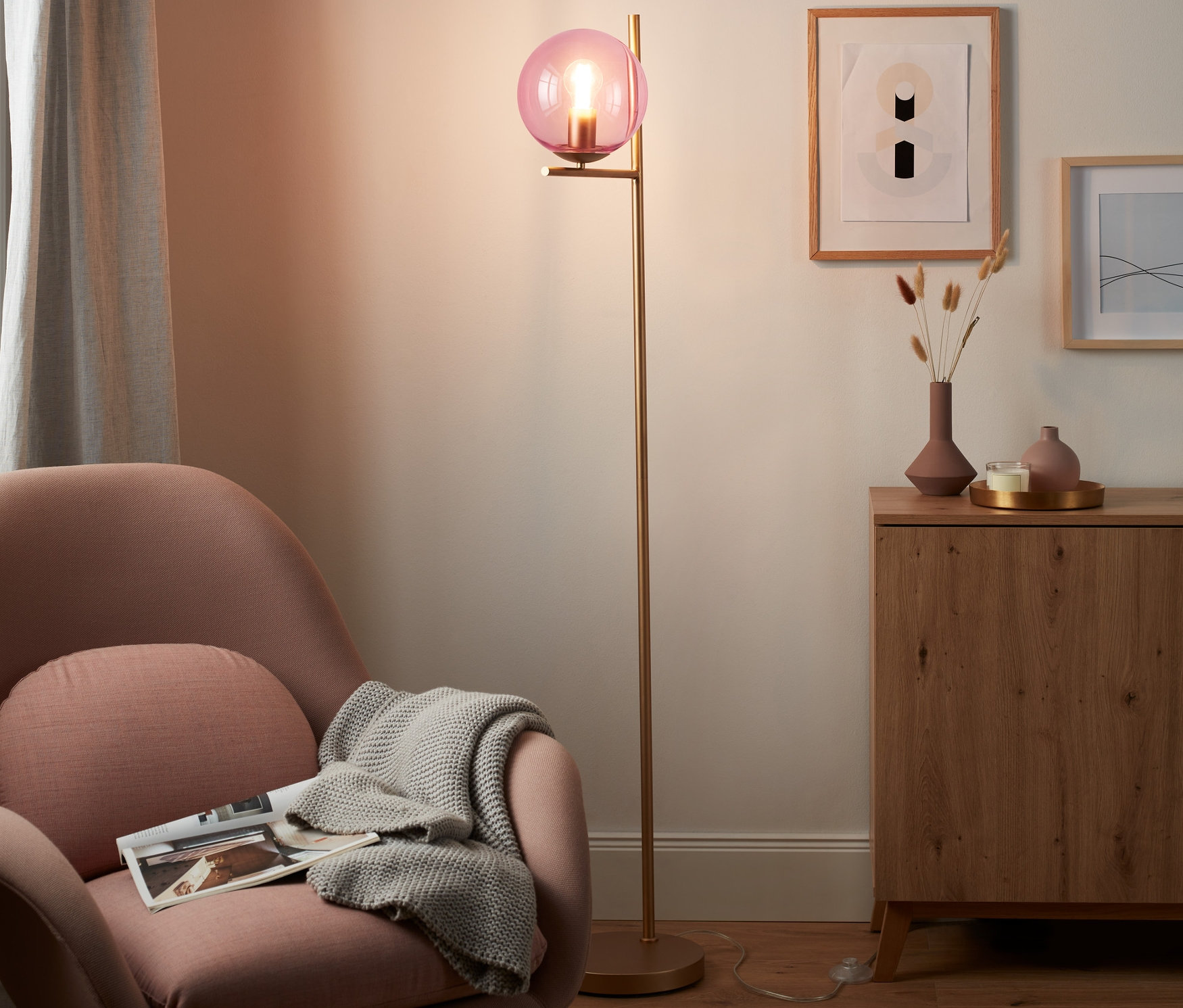 Różowy fotel z kocem i lampa stojąca »szklana kula« w salonie.