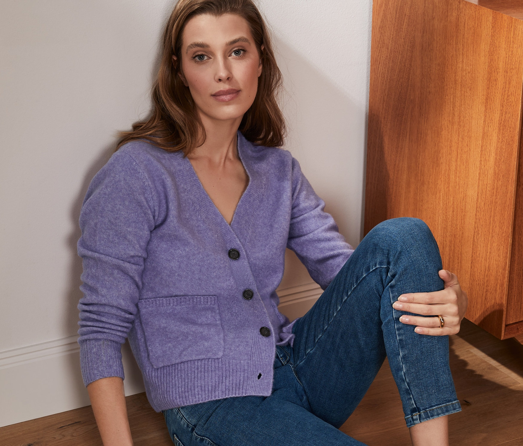 Kobieta siedzi na podłodze i ma na sobie liliowy sweter z dzianiny z wełną.