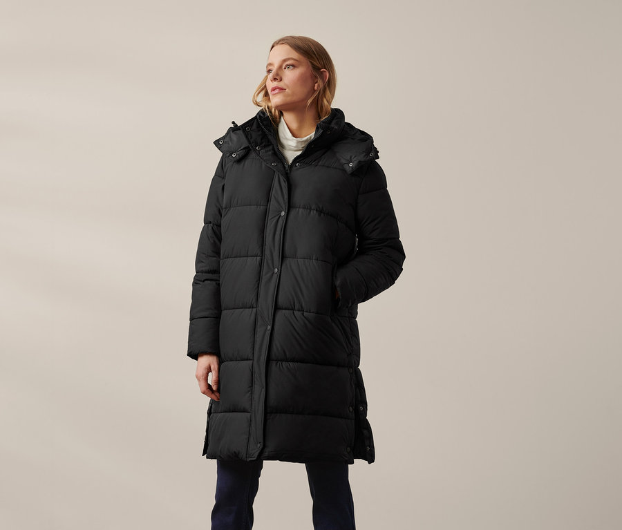 Kobieta ma na sobie czarny płaszcz pikowany z kapturem.