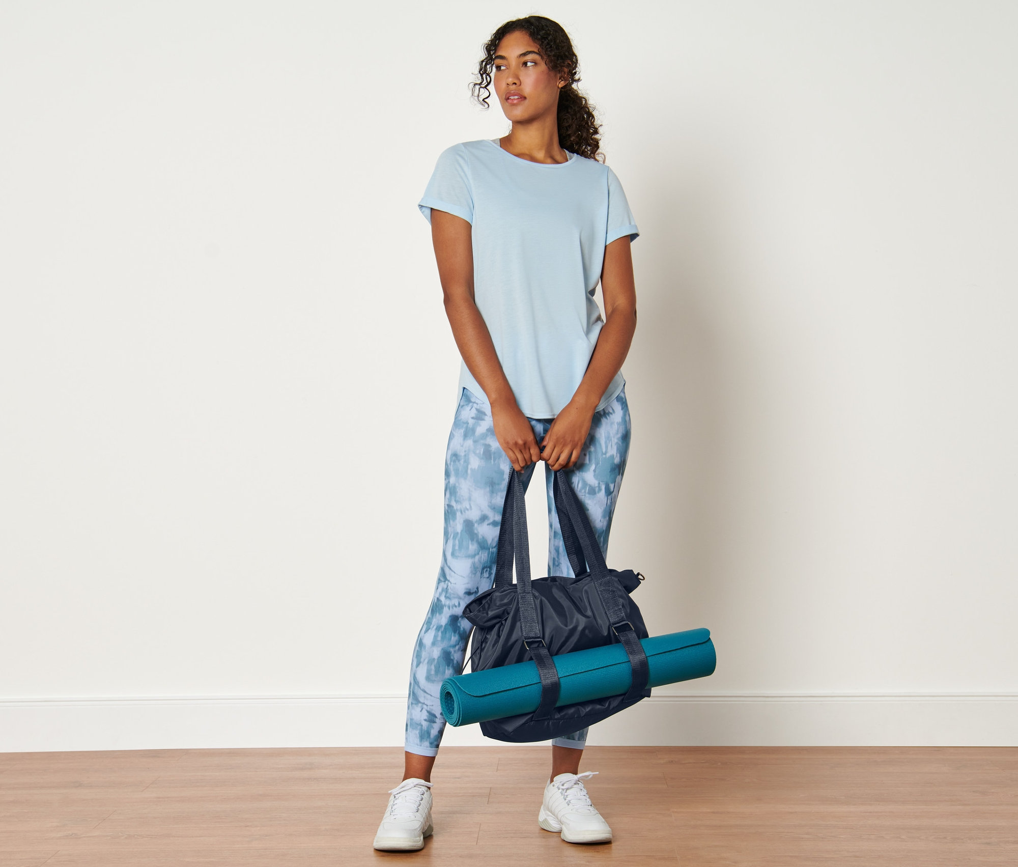 Kobieta trzyma torbę sportową i matę do jogi.