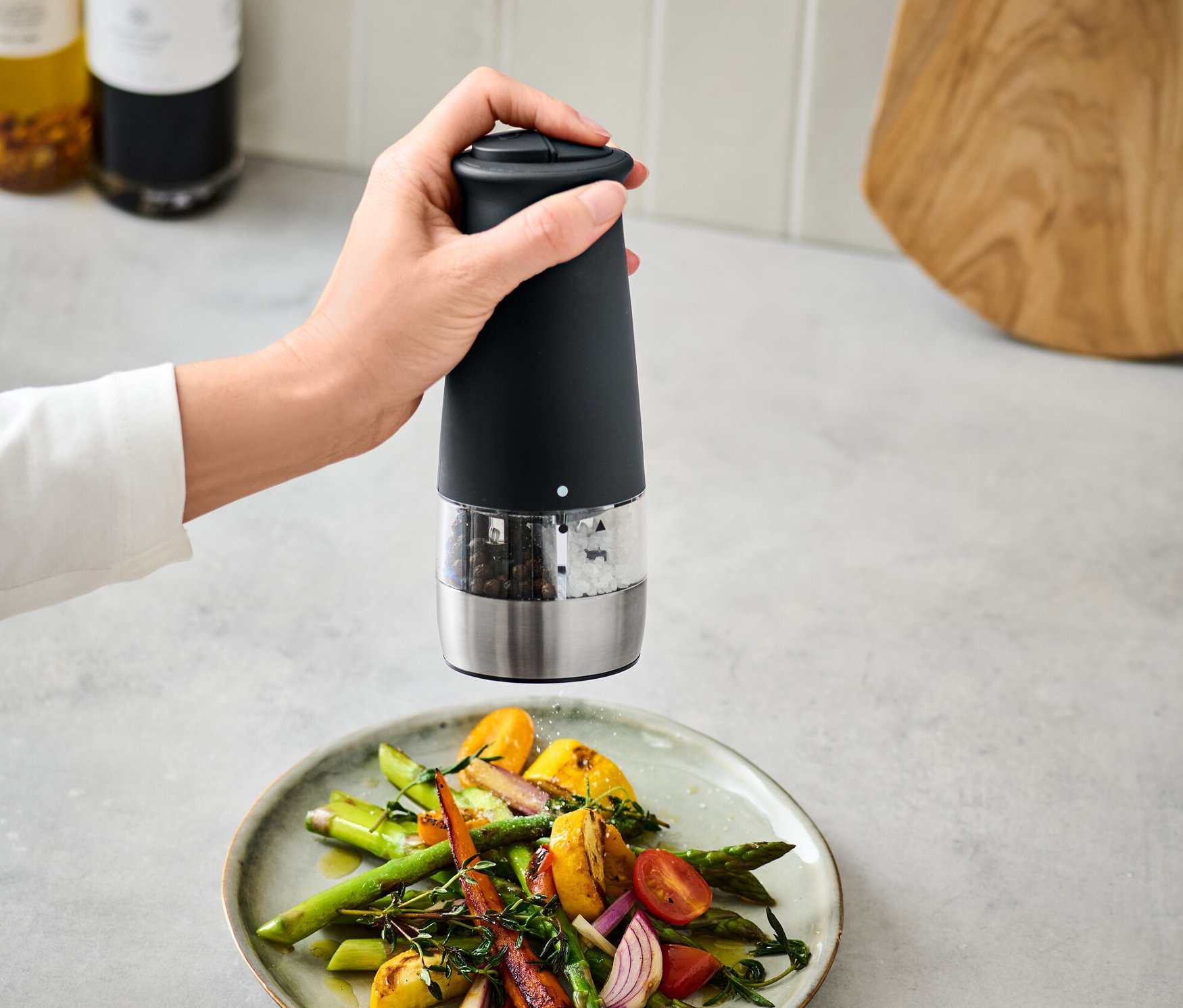 Ręka używa elektrycznego młynka do soli i pieprzu 2 w 1 nad talerzem warzyw.