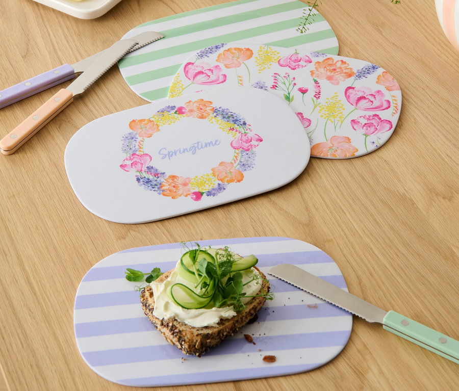 Cztery deski śniadaniowe z różnymi wzorami, nóż do masła i chleb z serem i ogórkiem na drewnianym stole.