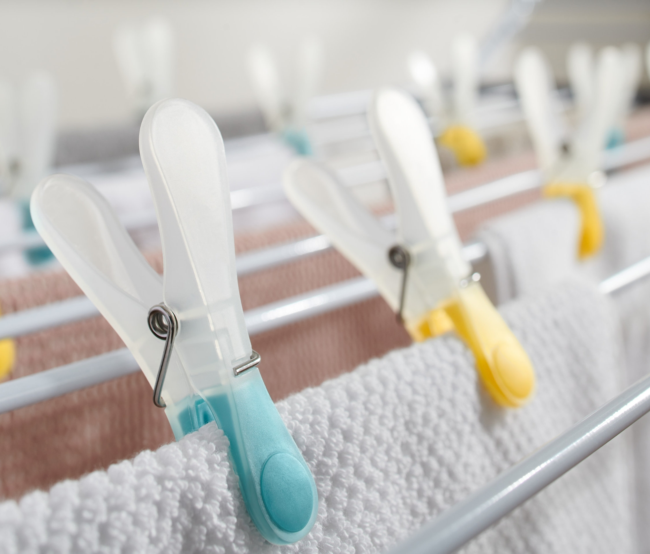Szczegół białej suszarki na bieliznę z kolorowymi Klamerki do bielizny, 20 sztuk, trzymającymi białe i różowe pranie.