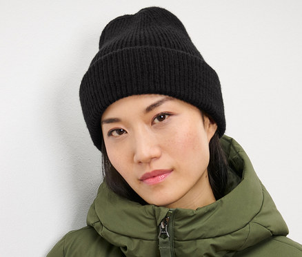 Kobieta ma na sobie czarną czapkę z dzianiny i zieloną kurtkę.