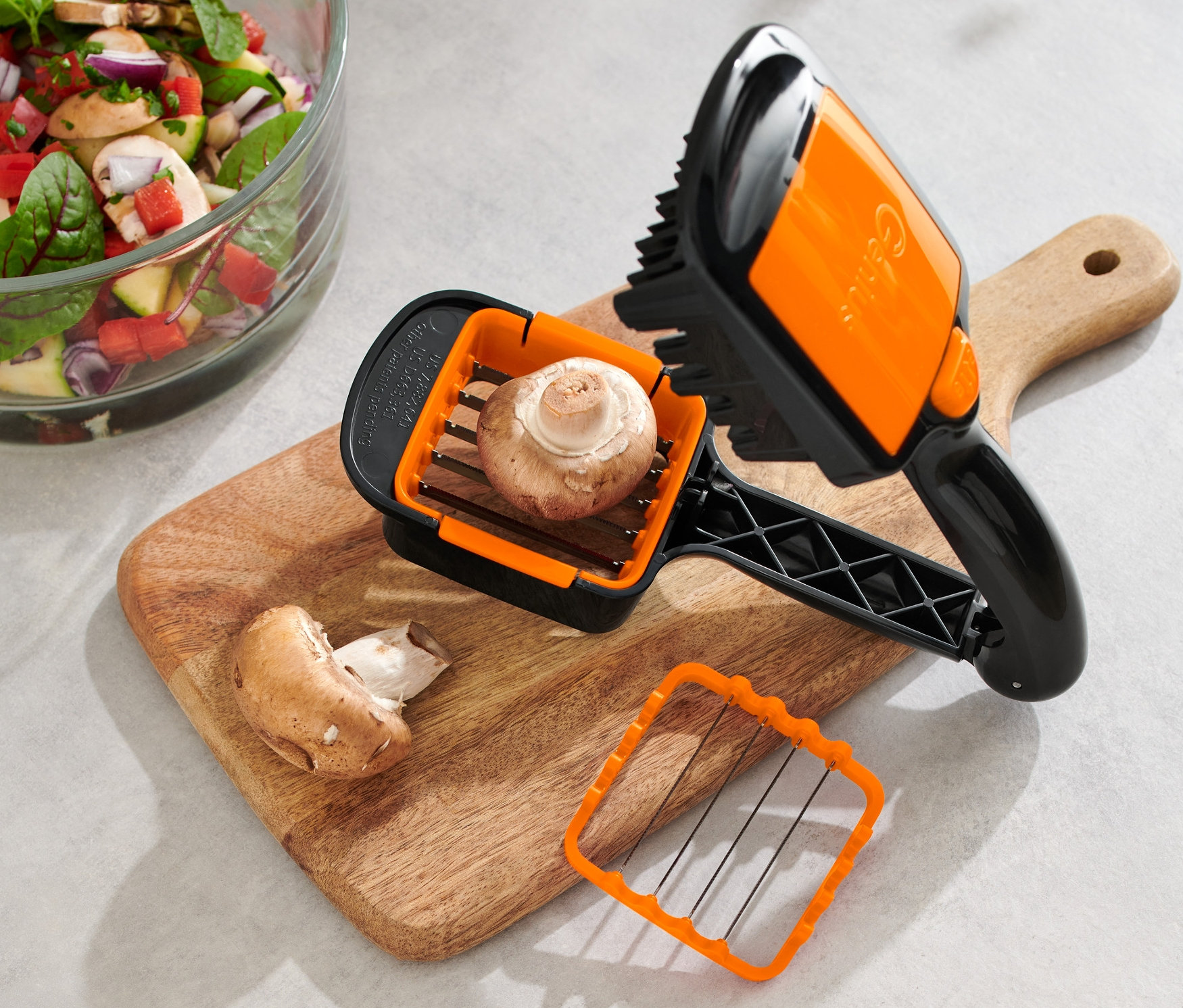 Grzyb w krajalnicy Nicer Dicer Quick XXL, 4-częściowy, na desce do krojenia obok sałatki.