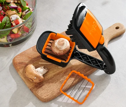 Grzyb w krajalnicy Nicer Dicer Quick XXL, 4-częściowy, na desce do krojenia obok sałatki.