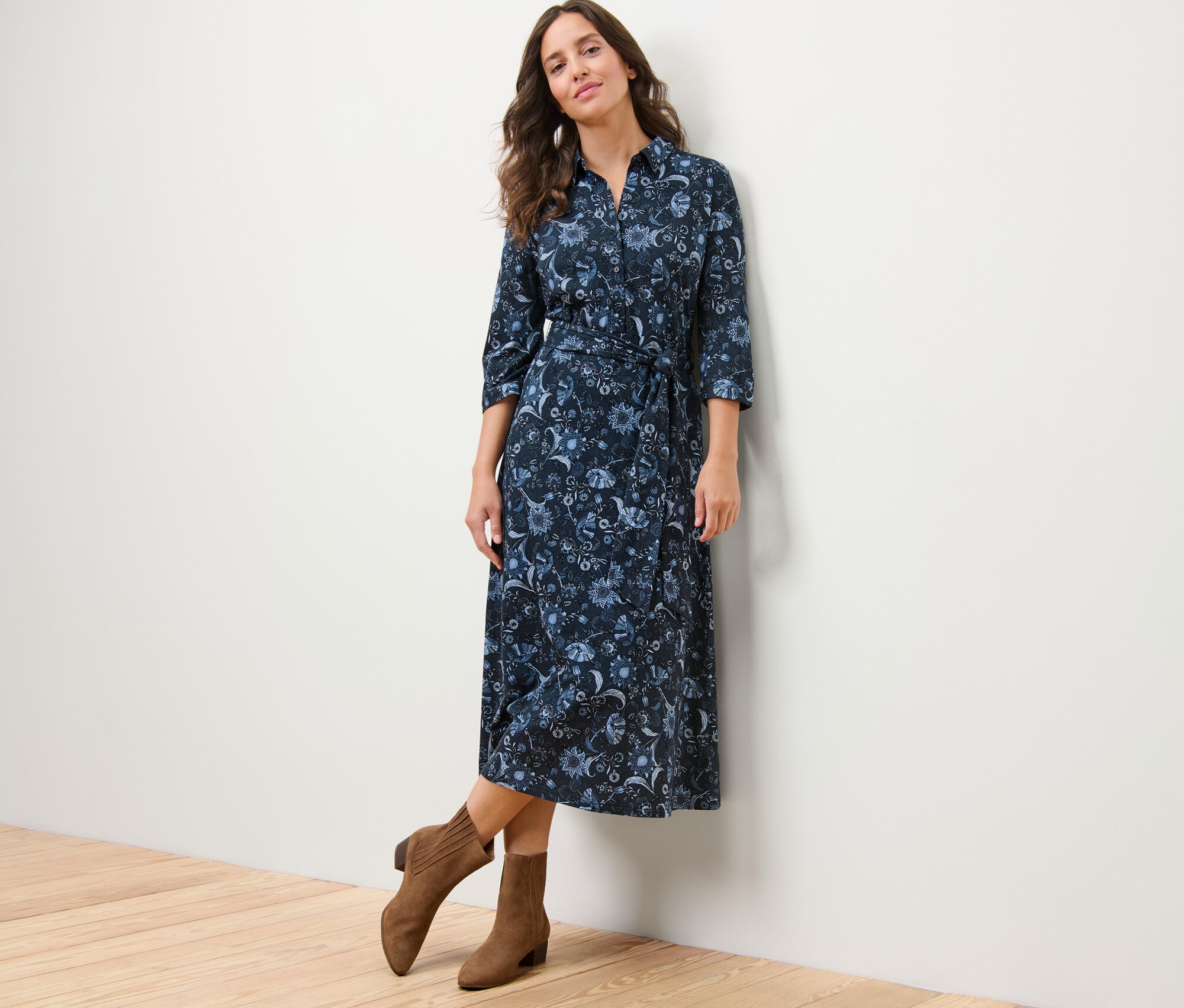 Kobieta pozuje w wzorzystej sukience z dżerseju i brązowych kozakach.