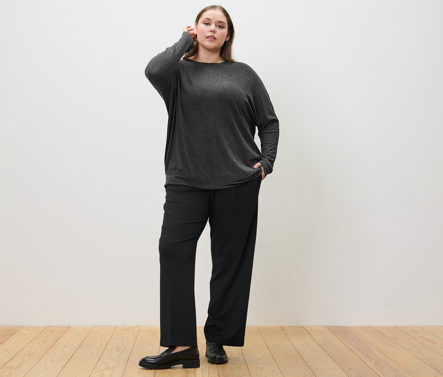 Kobieta pozuje w wygodnych spodniach z dżerseju i bluzce z rękawami typu nietoperz.