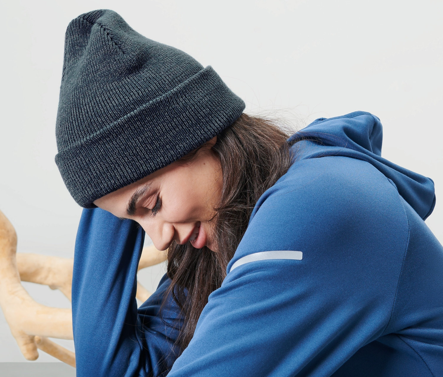 Kobieta siedzi i ma na sobie niebieską czapkę z dzianiny.