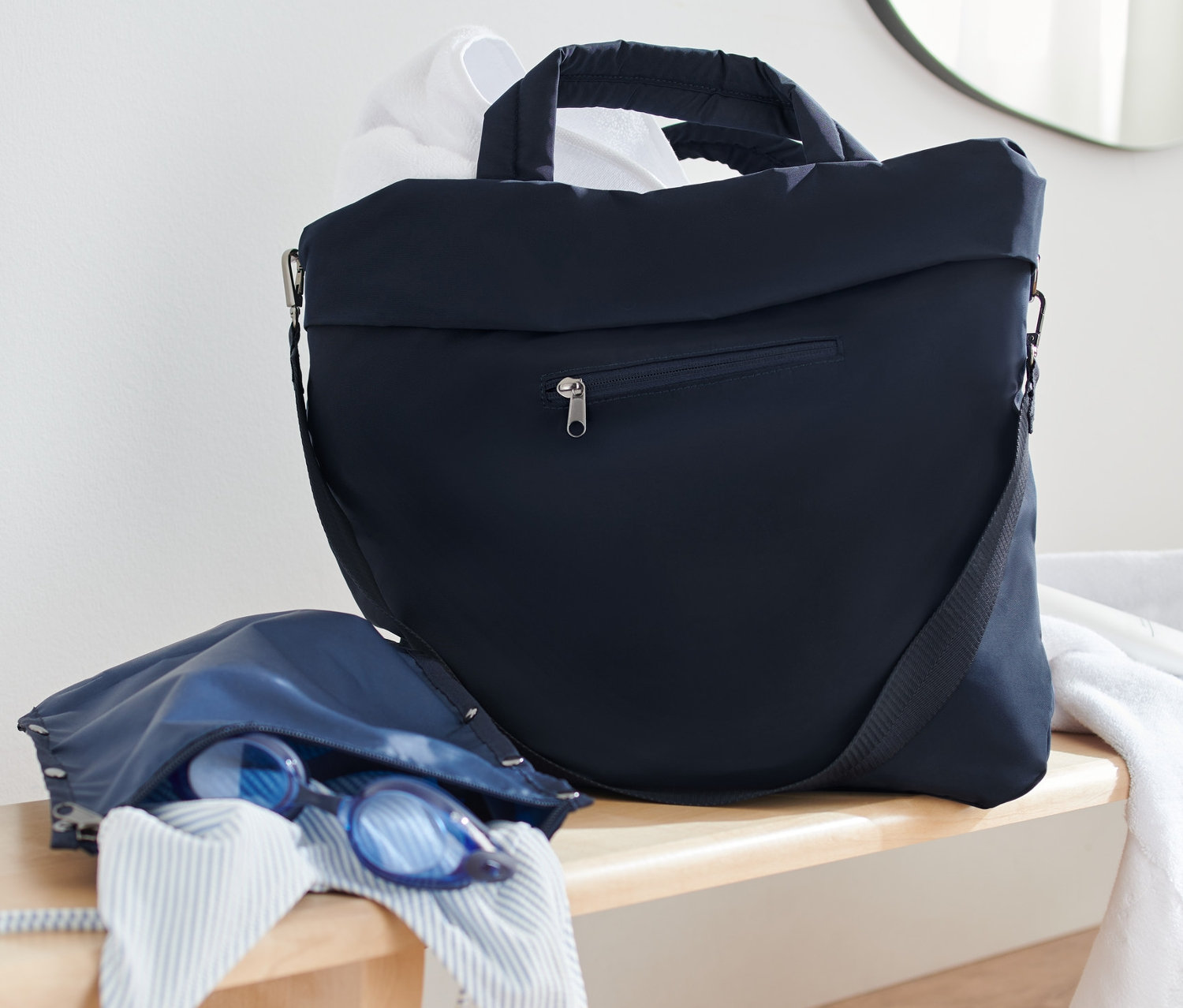 Granatowa torba sportowa i torba plażowa leżą na drewnianej ławce obok białego ręcznika.