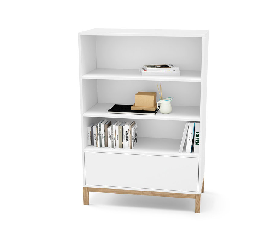 Biały regał z szufladą i półkami, na których leżą książki i dekoracje.