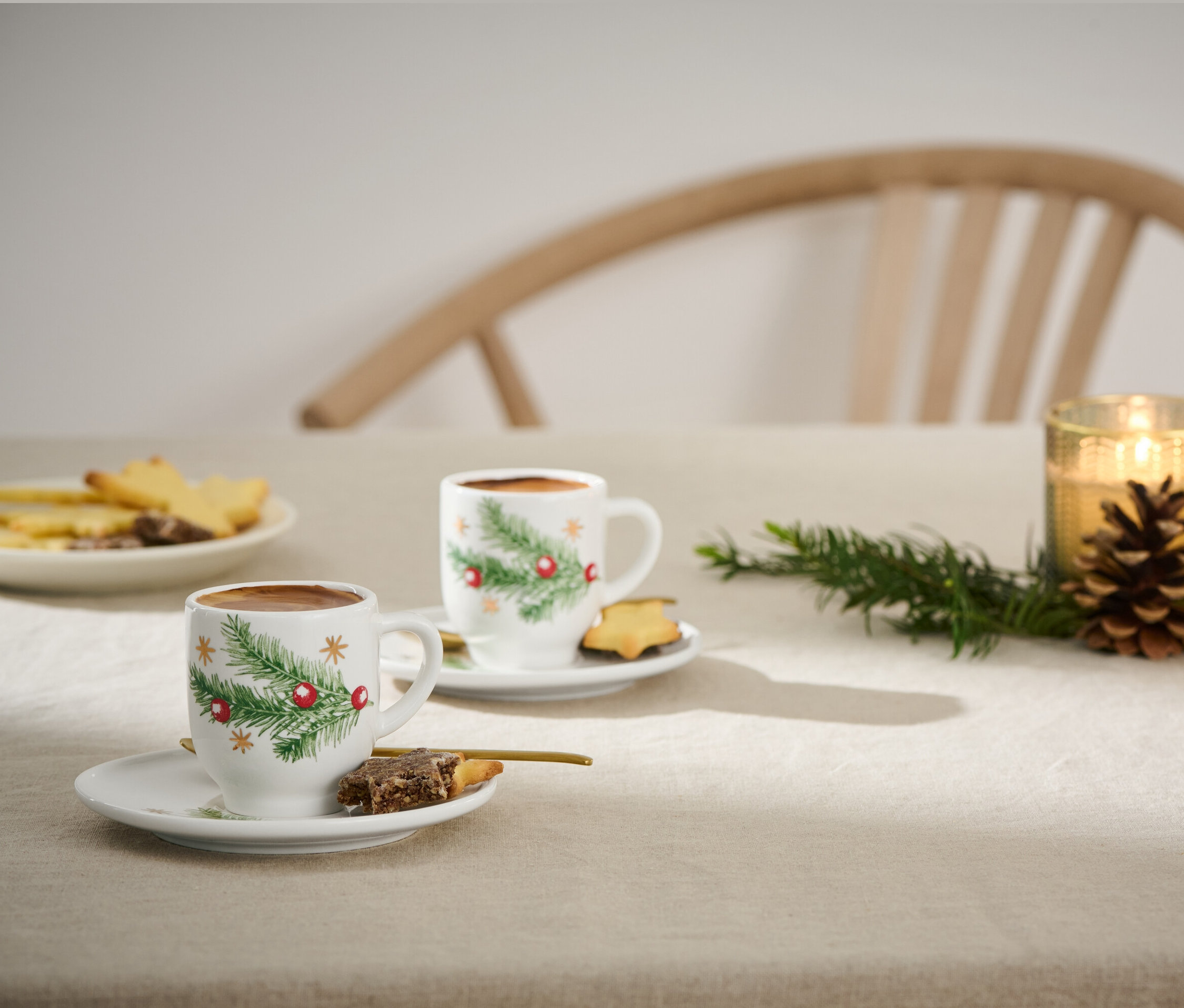 Dwie filiżanki do espresso z motywem świątecznym na stole z ciastkami i świecami.