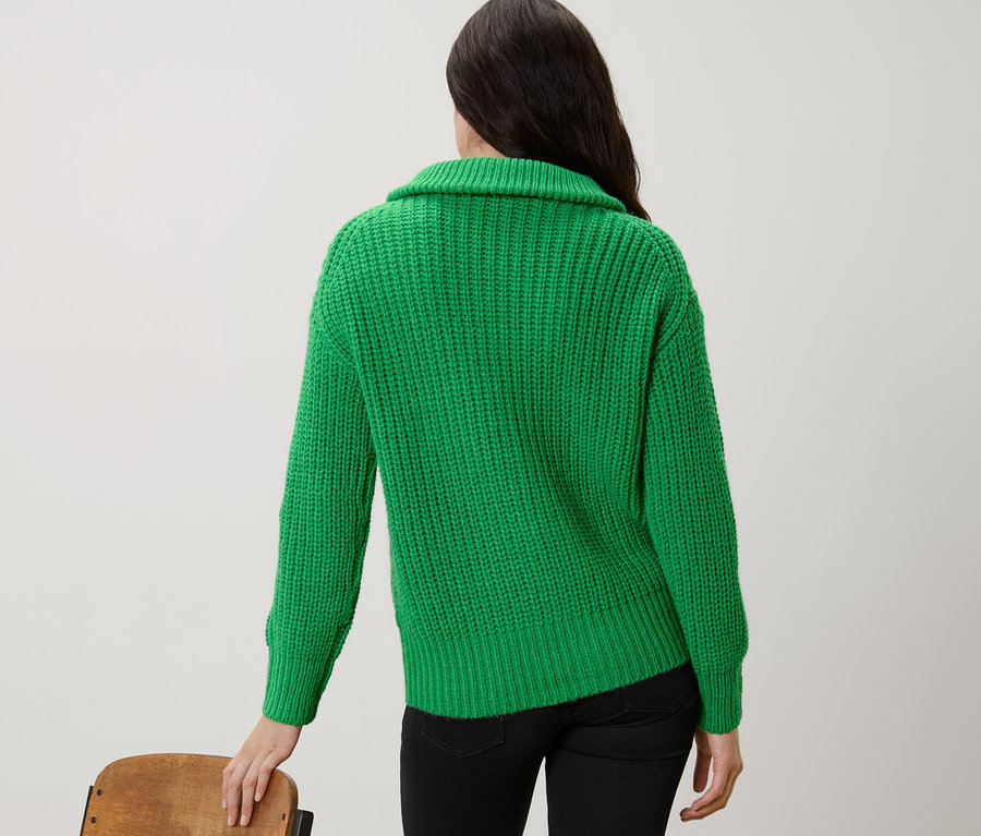 Kobieta stoi tyłem w zielonym swetrze o grubym splocie z kołnierzem typu troyer.