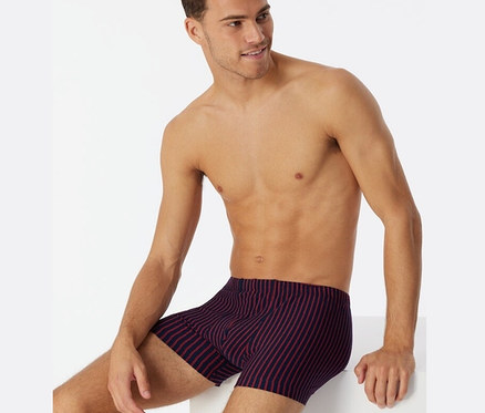 Mężczyzna siedzi i ma na sobie czerwone bokserki z bawełny ekologicznej SCHIESSER.