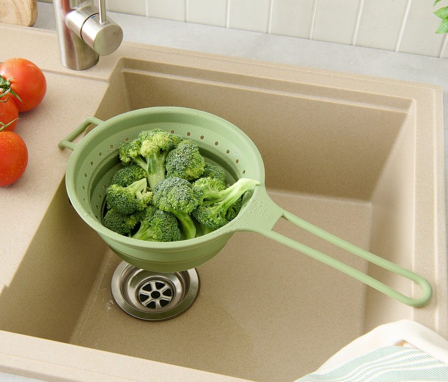 Brokuły w zielonym składanym sitku w beżowym zlewie z pomidorami i ziołami.